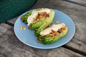 photo of Grilled Gem Lettuce with Caesar dressing, pine nuts and bacon on a grey plate